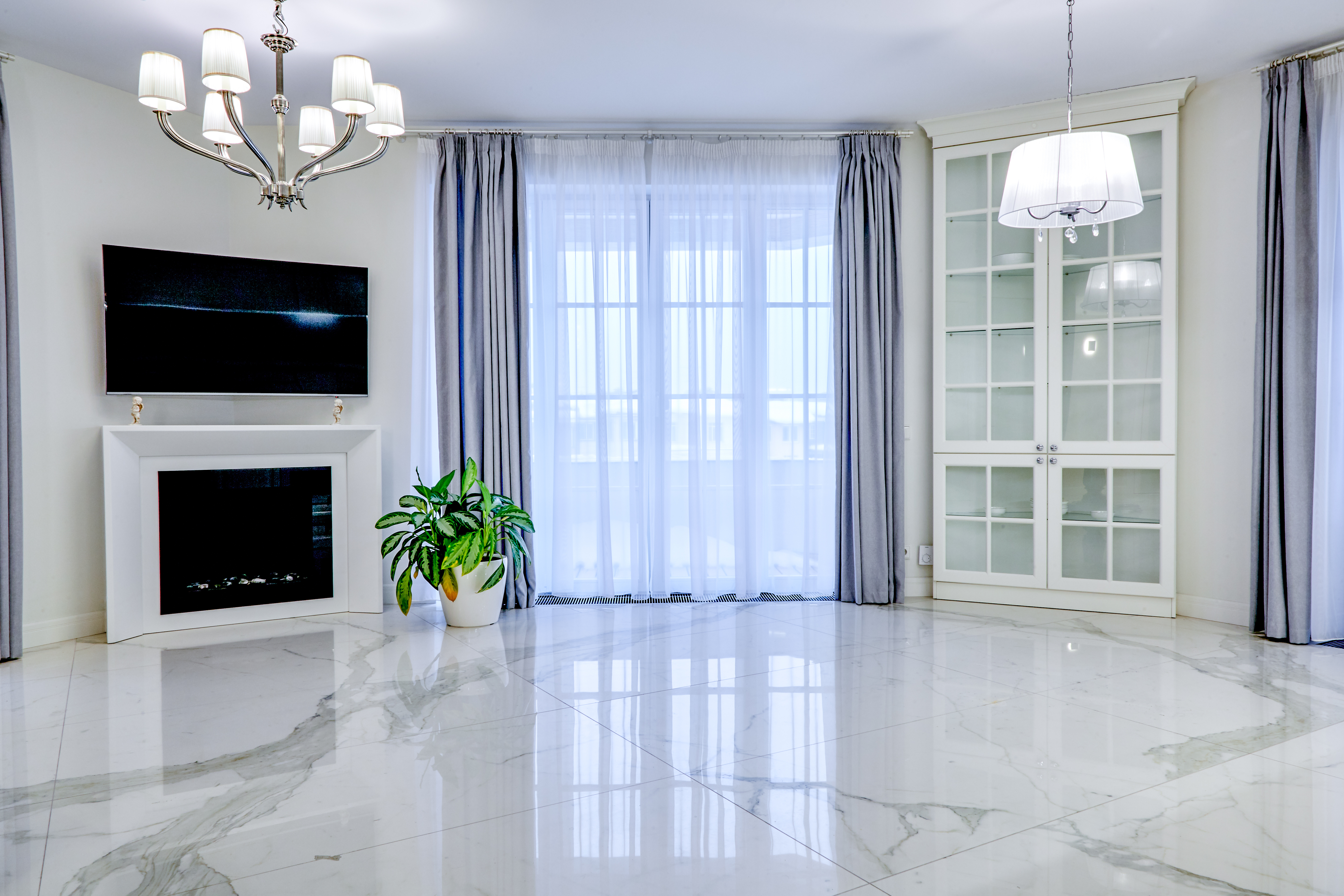 Modern living room with marble flooring, fireplace, TV, blue curtains, and glass cabinet doors